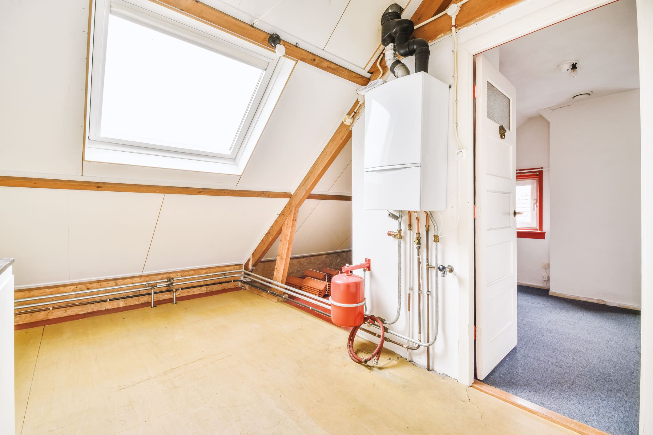 Boiler with pipes and gas cylinder in small empty mansard room with windows in modern apartment