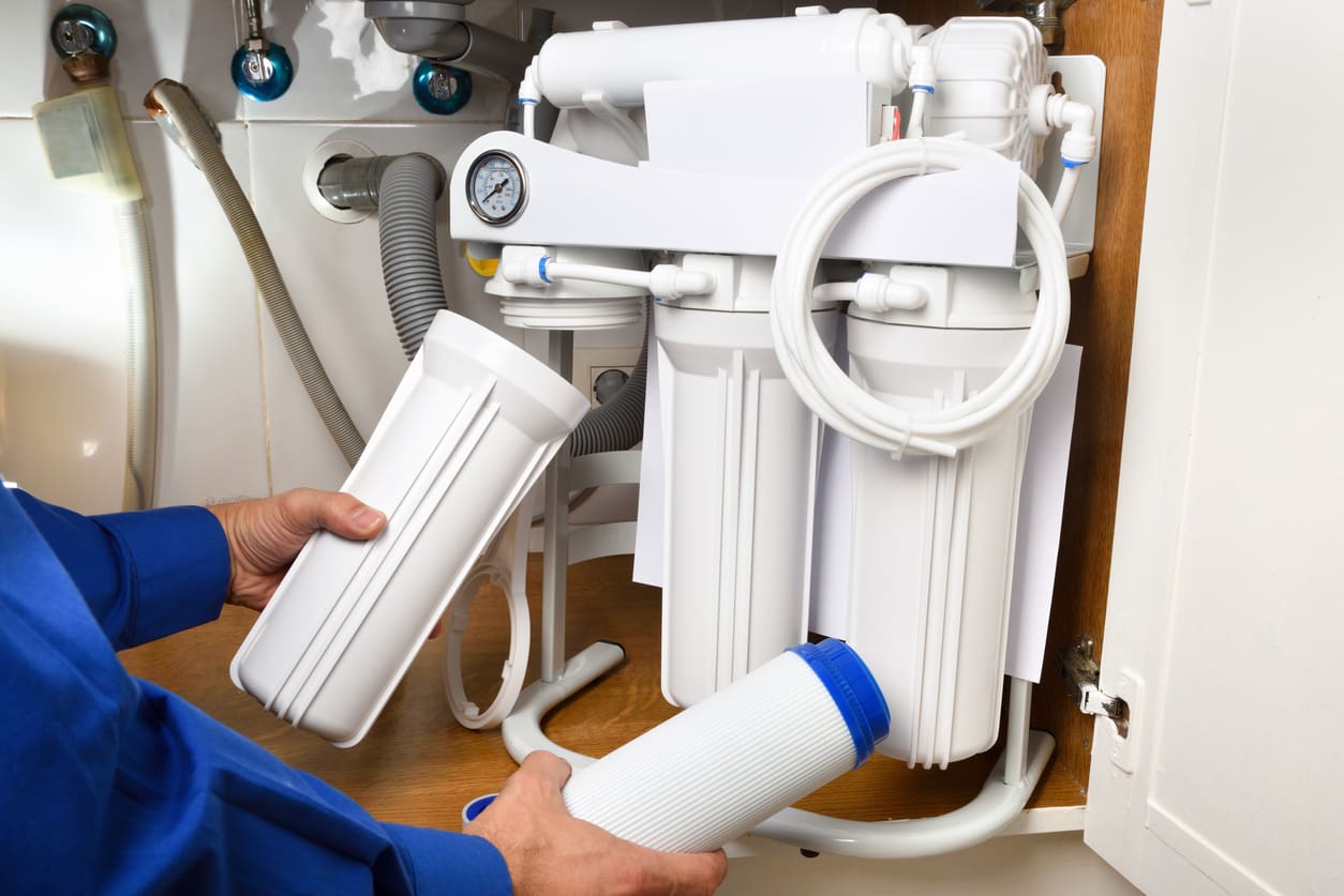 Technician installing reverse osmosis equipment under the sink close up. Front view. Horizontal composition.